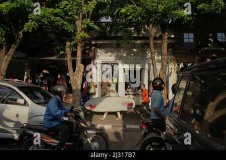 Ein junger Mann, der auf einem Bürgersteig vor den Geschäften an der Straße läuft und Surfbrett im Vordergrund der Verkehrsstaus in Legian, Kuta, Badung, Bali, Indonesien trägt. Bali wurde im März 2022 für Touristen wiedereröffnet, nachdem es aufgrund von Covid-19 fast zwei Jahre lang geschlossen wurde, da geimpfte Reisende bei der Ankunft nicht mehr in Quarantäne gehen müssten, was die Hoffnung auf vom Tourismus abhängige Dörfer, die von wirtschaftlichen Verlusten betroffen sind, verstärkt. © Reynold Sumayku Stockfoto