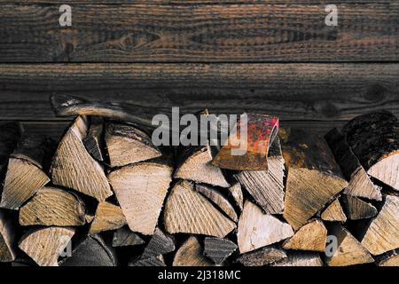 Brennholzstapel mit Axt vor Holzwand Stockfoto