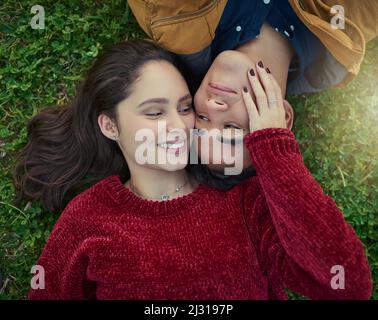 Mit dir neben mir ist das Leben komplett. High-Angle-Aufnahme eines glücklichen jungen Paares, das zusammen auf dem Gras liegt. Stockfoto