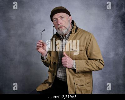 Zwangloses Studioporträt eines bärtigen älteren Mannes mit Brille und Hafenmütze Stockfoto