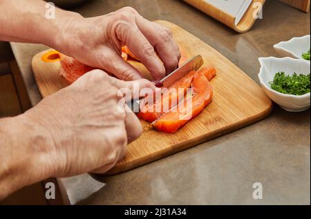 Der Koch schneidet den Lachs mit einem Messer in Streifen, um das Gericht gemäß dem Rezept zuzubereiten Stockfoto