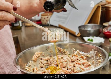 Der Koch gießt Olivenöl aus der Flasche in ein Gericht mit Lachs Stockfoto