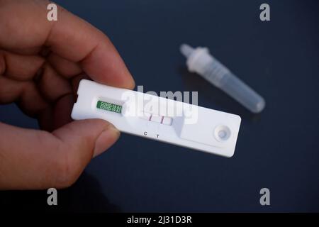 Menschliche Hand zeigt eine Covid-19-Kassette mit positiven Ergebnissen aus einem Rapid-Antigen-Test-Kit (ATK) Stockfoto