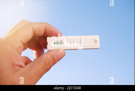 Eigene Hand mit negativem Covid-19-Testergebnis mit SARS CoV-2 Rapid Antigen Test Kit (ATK) und blauem Himmel-Hintergrund mit Sonnenlicht, Coronavirus-Infecti Stockfoto