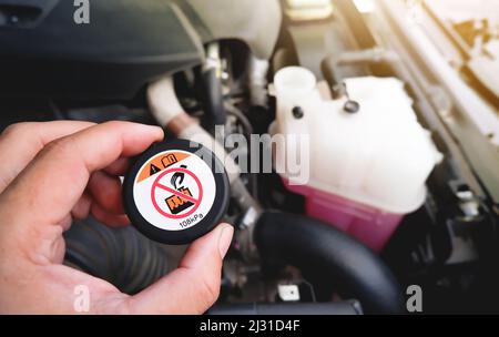 Eine mechanische Hand hält einen Kühlerdeckel mit einem Warnhinweis für hohe Temperaturen fest. Stockfoto