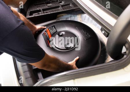 Ein Mechaniker installiert einen Donut-förmigen Treibgastank in einem Reserveradloch in einer Autowerkstatt Stockfoto