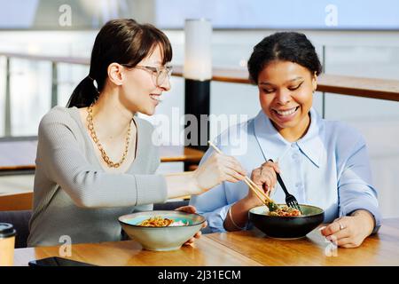 Portrait von zwei jungen Mädchen, die im Café asiatisches Essen genießen und fröhlich das Essen teilen Stockfoto