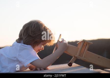 Kleiner Junge mit Holzflugzeug, Junge will Pilot und Astronaut werden. Glückliches Kind spielen mit Spielzeug Flugzeug. Kinderpilot träumt vom Fliegen. Kindheit Stockfoto