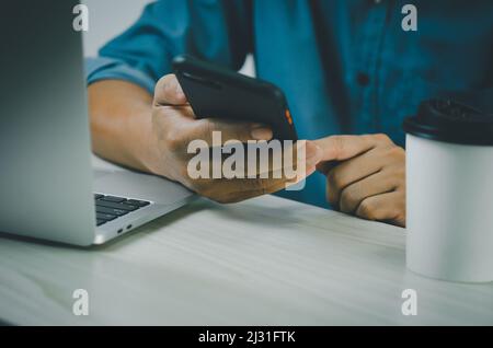 Mann Hand hält Smartphone und Computer-Laptop, um die Arbeitstechnologie Internet suchen, SMS senden, mit SMS-Messenger oder Online-Banking. Stockfoto