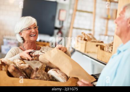 Ich hoffe, es gefällt Ihnen, weil ich es gerne gebacken habe. Aufnahme einer glücklichen älteren Frau, die einen Kunden in einer Bäckerei bedient. Stockfoto