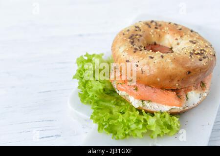 Frisches, mehrkörniges Bagel-Brötchen mit Frischkäse, geräucherten Lachsscheiben, Dill und grünem Salat, Nahaufnahme Stockfoto