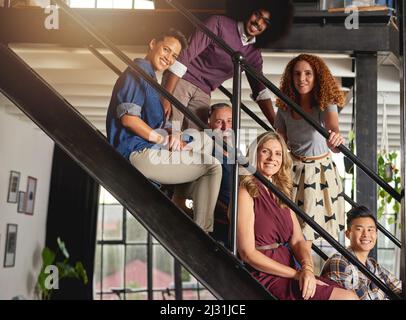 Die Treppe zum kreativen Erfolg ist ein flippiges. Porträt einer Gruppe von kreativen Mitarbeitern, die in einem modernen Büro auf einer Treppe sitzen. Stockfoto