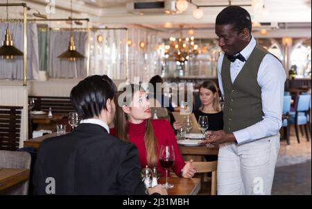 Ein positives Paar, das mit einem afroamerikanischen Kellner sprach Stockfoto