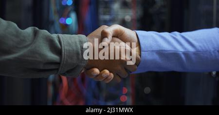 Gute Arbeit. Eine kurze Aufnahme von zwei nicht erkennbaren männlichen IT-Support-Mitarbeitern, die sich in einem dunklen Netzwerkserverraum die Hände schüttelten. Stockfoto