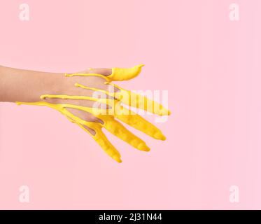 Kreatives Konzept einer erhobenen Hand, die in gelbe Farbe in die Luft getaucht wurde. Pastellrosa Hintergrund. Stockfoto