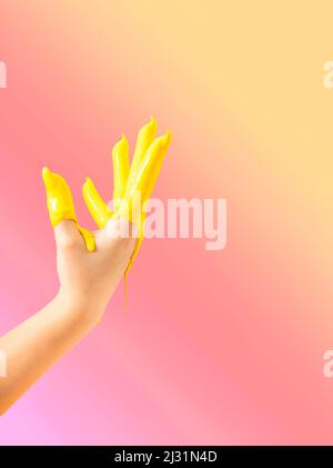 Kreatives Konzept einer erhobenen Hand, die in gelbe Farbe in die Luft getaucht wurde. Pastellfarbener neonpinker Hintergrund. Stockfoto