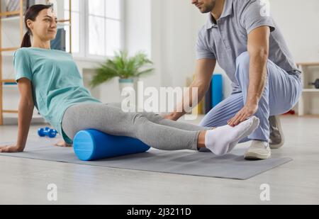 Physiotherapeutin schult junge Frau mit Schaumstoffwalze im modernen Rehabilitationszentrum. Stockfoto