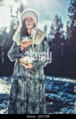 Schöne schamanische Mädchen spielen auf tibetische Schüssel in der Natur. Stockfoto