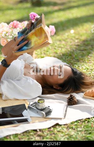 Die schöne asiatische Frau aus der Nähe liest gerne ein Buch und legt sich im Park auf eine Picknickdecke. Stockfoto