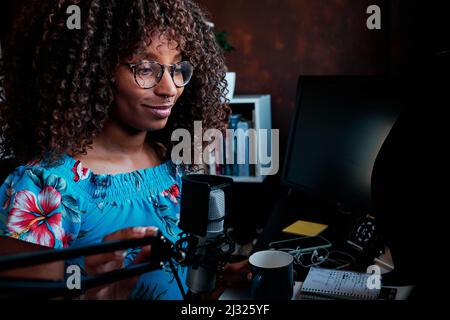 Junge lockige Haare schwarze Frau Podcasting mit Mikrofon am Computer Stockfoto