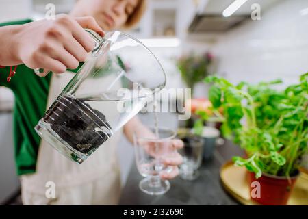 Mädchen gießt Wasser aus dem Glas mit Schungitsteinen Stockfoto