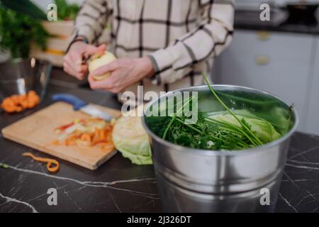 Frau wirft Gemüseschnitzel in einen Komposteimer in der Küche. Stockfoto