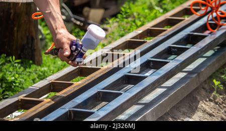 Ein Mann mit einem Farbsprüher malt eine Metallstruktur auf der Straße. Selektiver Fokus Stockfoto