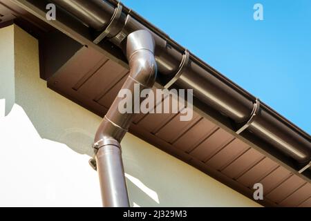 Braune pvc-Dachrinne mit Fallrohr am Dachrand und Himmel verbunden. Stockfoto