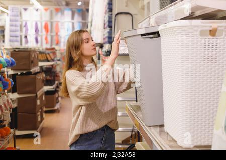 Die junge Frau in einem Haushaltsladen wählt einen Stoffkorb für schmutzige Wäsche. Stockfoto