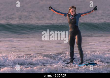 Eine junge Surferin feiert ihr erstes Mal, dass sie auf einem Surfbrett am Fistral Beach in Newquay in Cornwall in Großbritannien aufsteht. Stockfoto