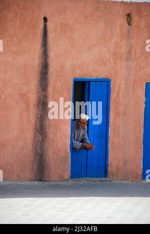 Ein Mann ruht sich an seiner Eingangstür in den Straßen der Medina in Marrakesch aus Stockfoto