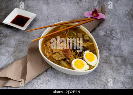 Große Schüssel mit japanischer Miso-Suppe von Ramen mit Gemüse und Fleisch, begleitet von Sojabohnen auf grauem Steingrund Stockfoto