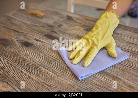 Die Hand eines Mannes in einem medizinischen Handschuh wischt den Tisch mit Serviette ab. Hintergrund Kellner in einer Schürze in Unschärfe. Oberflächenbehandlung Stockfoto