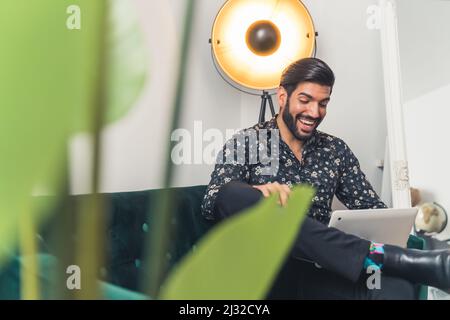 Gutaussehender lateinischer Mann, der per Videoanruf mit dem Laptop auf dem Sofa sitzt - Remote Meeting . Hochwertige Fotos Stockfoto