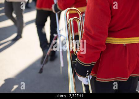 Orchestermitglied hält Messingpfeife. Details zum Trompeter. Zeremonielle rote Uniform. Militärkapelle auf der Straße. Stockfoto