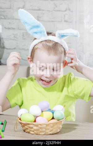 Osterkinder. Glücklicher Junge in Kaninchenohren auf dem Kopf spielt zu Hause mit bunten Eiern. Vorbereitung auf die Easter die große Eiersuche. Osterhase. Ostereier. Stockfoto