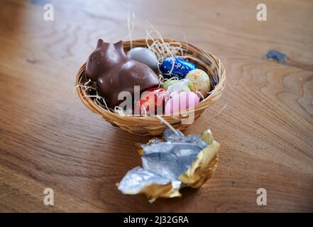 PRODUKTION - 01. April 2022, Berlin: ILLUSTRATION - Ein zerbrochener Schokoladenhase liegt mit Eiern in einem Osternest. Die Umhüllung liegt daneben. (Posierte Szene) Foto: Annette Riedl/dpa Stockfoto