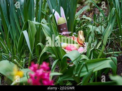 PRODUKTION - 01. April 2022, Berlin: ILLUSTRATION - ein Osternest mit gebranntem Hase, Schokoladenhase, farbigen Eiern und Schokoladeneiern liegt in einem Blumenbeet. (Posierte Szene) Foto: Annette Riedl/dpa Stockfoto