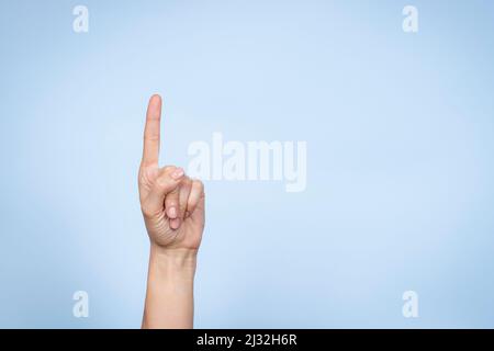 Handbewegung. Weibliche Hand zeigt die Nummer eins. Frau zeigt mit Zeigefinger auf hellblauen Hintergrund Stockfoto