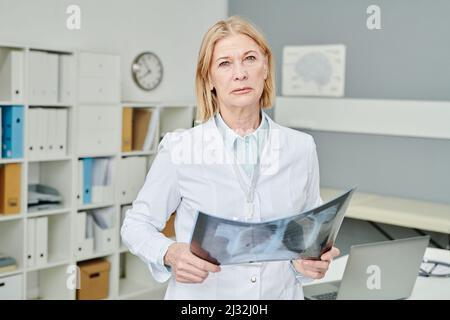 Radiologe in Whitecoat hält Röntgenbild der Lunge, während er die Diagnose für den Patienten nach dem Ergebnis der medizinischen Untersuchung festlegt Stockfoto