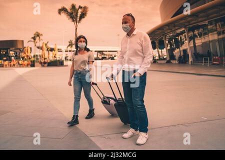 Ein paar Freunde in Schutzmasken plaudern, während sie den Flughafen mit ihrem Gepäck verlassen Stockfoto
