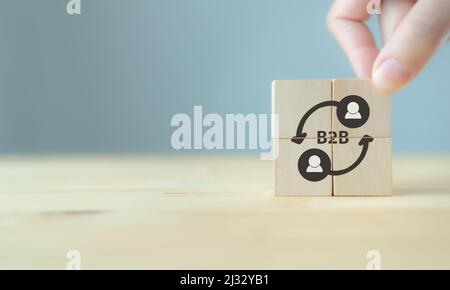 Business to Business, B2B, BTB-Marketingkonzept. Die Holzwürfel mit der Abkürzung B2B und dem Symbol auf grauem Hintergrund und Kopierraum in der Hand halten. Bus Stockfoto