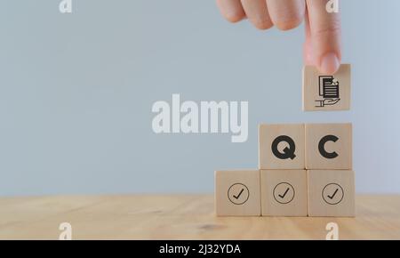 Qualitätskontrollkonzept (QC). Für Unternehmen und Industrie. Standardqualität, Garantie, Prozess, Prüfung und Genehmigung. Holzwürfel mit Guaran in der Hand halten Stockfoto