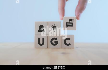 Nutzergeneriertes Content-Konzept.(UGC) Online-Marketing-Konzept. Kunden erstellen Inhalte auf Social Media . Hand aus der Nähe Legen Sie einen Holzwürfel mit dem Symbol „UGC“ auf Stockfoto