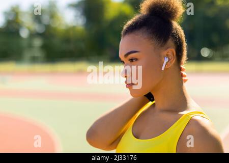 Sportliche schwarze Frau in gelber Sportkleidung, die Musik hört Stockfoto