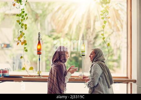 Bekommen ihren Kaffee und Mädchen reden fix. Aufnahme von zwei Frauen, die sich bei einem Kaffee in einem Café unterhalten. Stockfoto