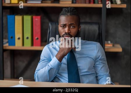Leidgelaunter männlicher Unternehmer, der in seinem Büro sitzt Stockfoto