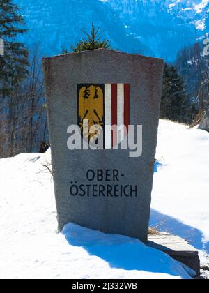 Steinerner Grenzposten von Oberösterreich mit seinem Wappen in Winterlandschaft mit Schnee. Stockfoto