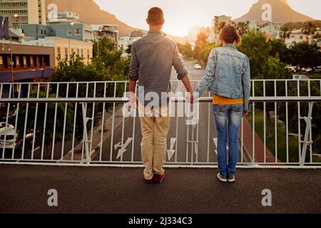 Urbane Liebe. Rückansicht eines Paares, das auf einer Stadtbrücke zusammenstand und die Aussicht betrat. Stockfoto