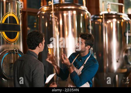 Es geht um den Geschmack. Aufnahme von zwei jungen Männern, die tagsüber ihre Biermaschine in einer Bierbrauerei inspizieren. Stockfoto